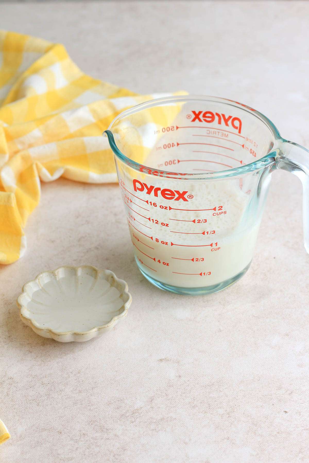 A liquid measuring cup with soy milk and a small dish of vinegar next to it.