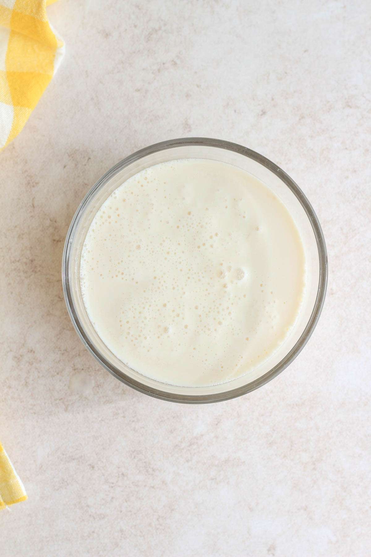 A small glass bowl with homemade vegan buttermilk on a tan counter.