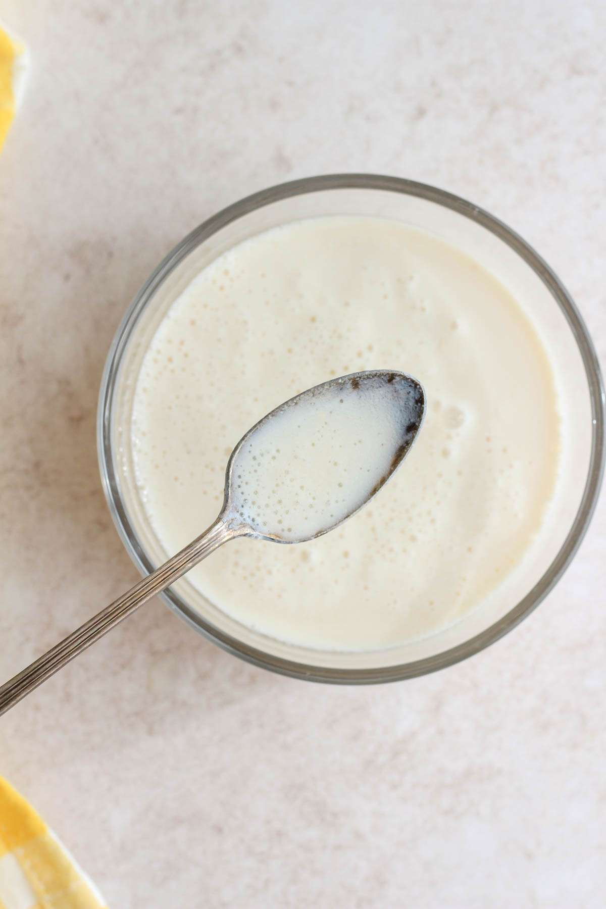 A glass bowl of vegan buttermilk with a silver spoon holding a scoop of buttermilk over the bowl.
