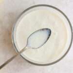 A small glass bowl of vegan soy buttermilk with a silver spoon scooping some out.