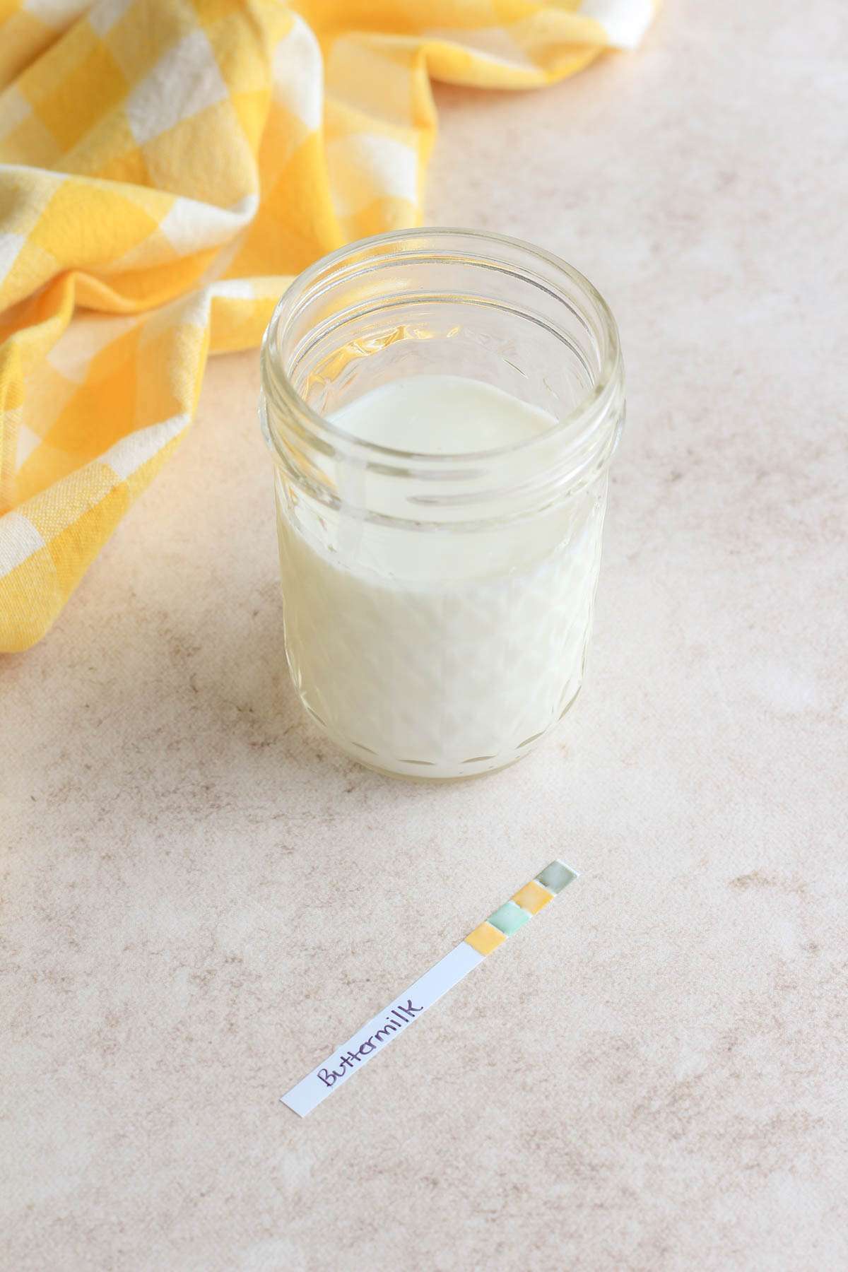 A mason jar with cultured buttermilk and a pH strip in front showing the pH of the buttermilk.