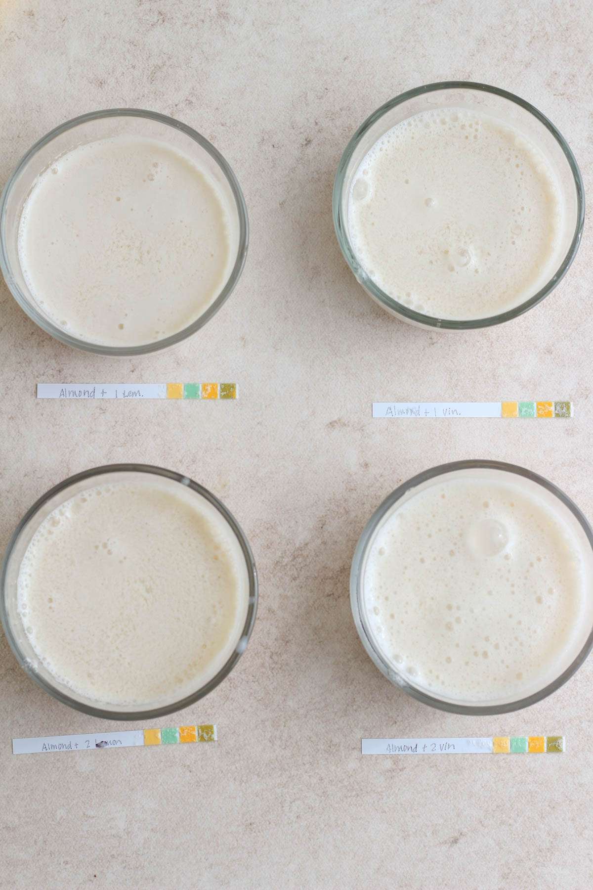 Almond milk in four bowls mixed with lemon or vinegar with pH strips in front.