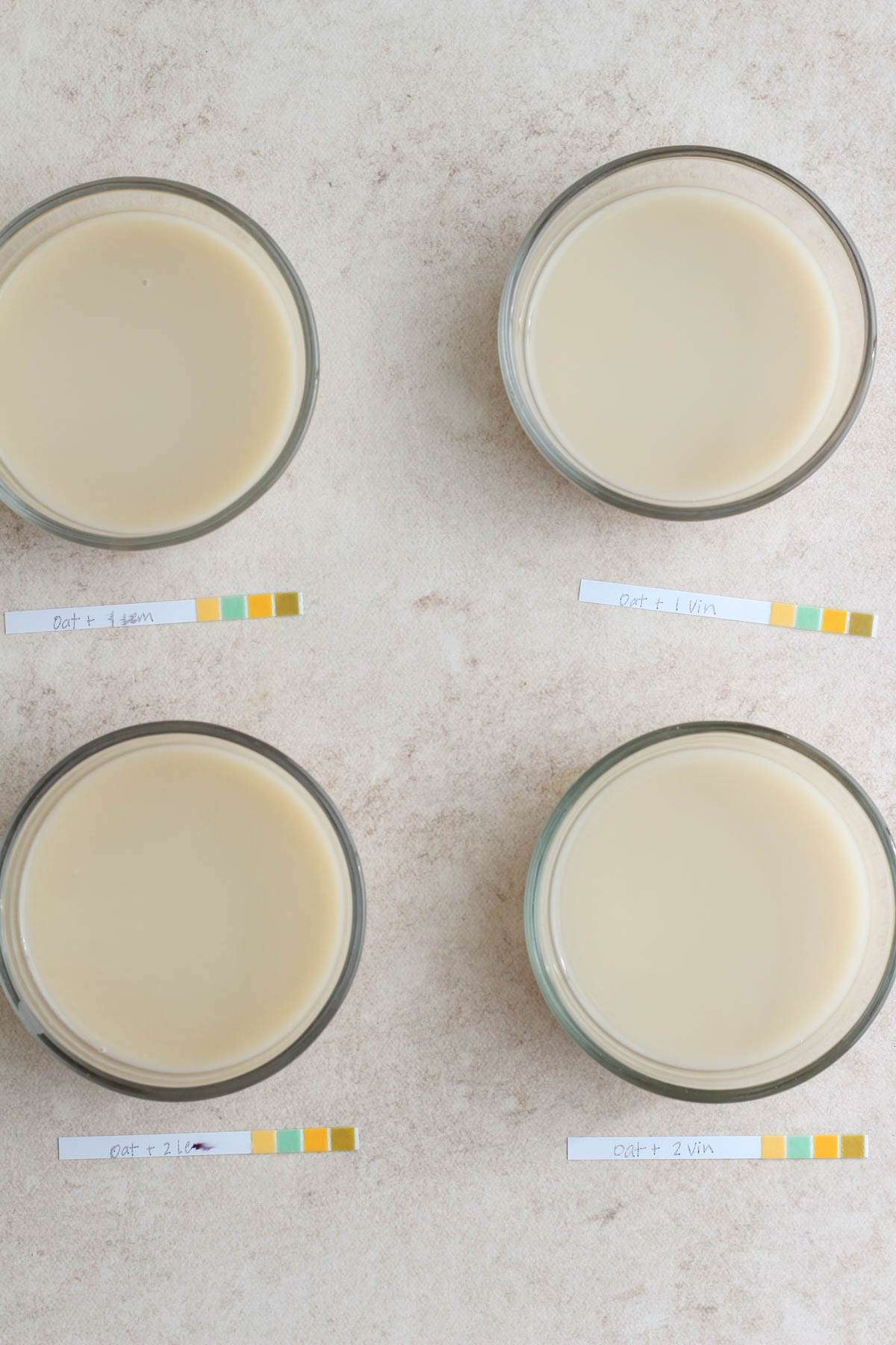 Oat milk in four bowls mixed with lemon or vinegar with pH strips in front.