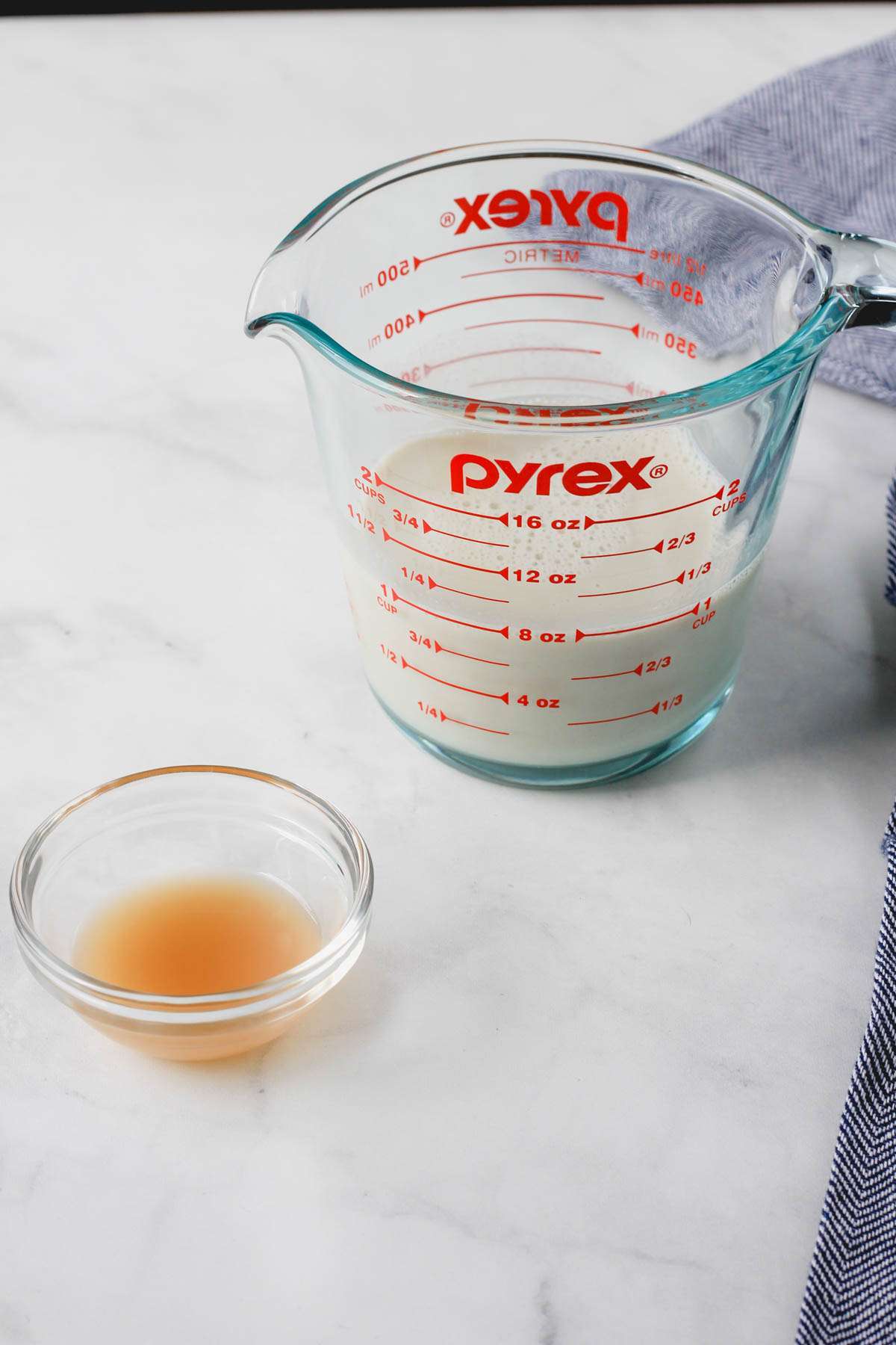A liquid measuring cup with non-dairy milk and a small bowl with apple cider vinegar to the left.