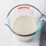 A close up of a liquid measuring cup with dairy-free buttermilk on a white counter.