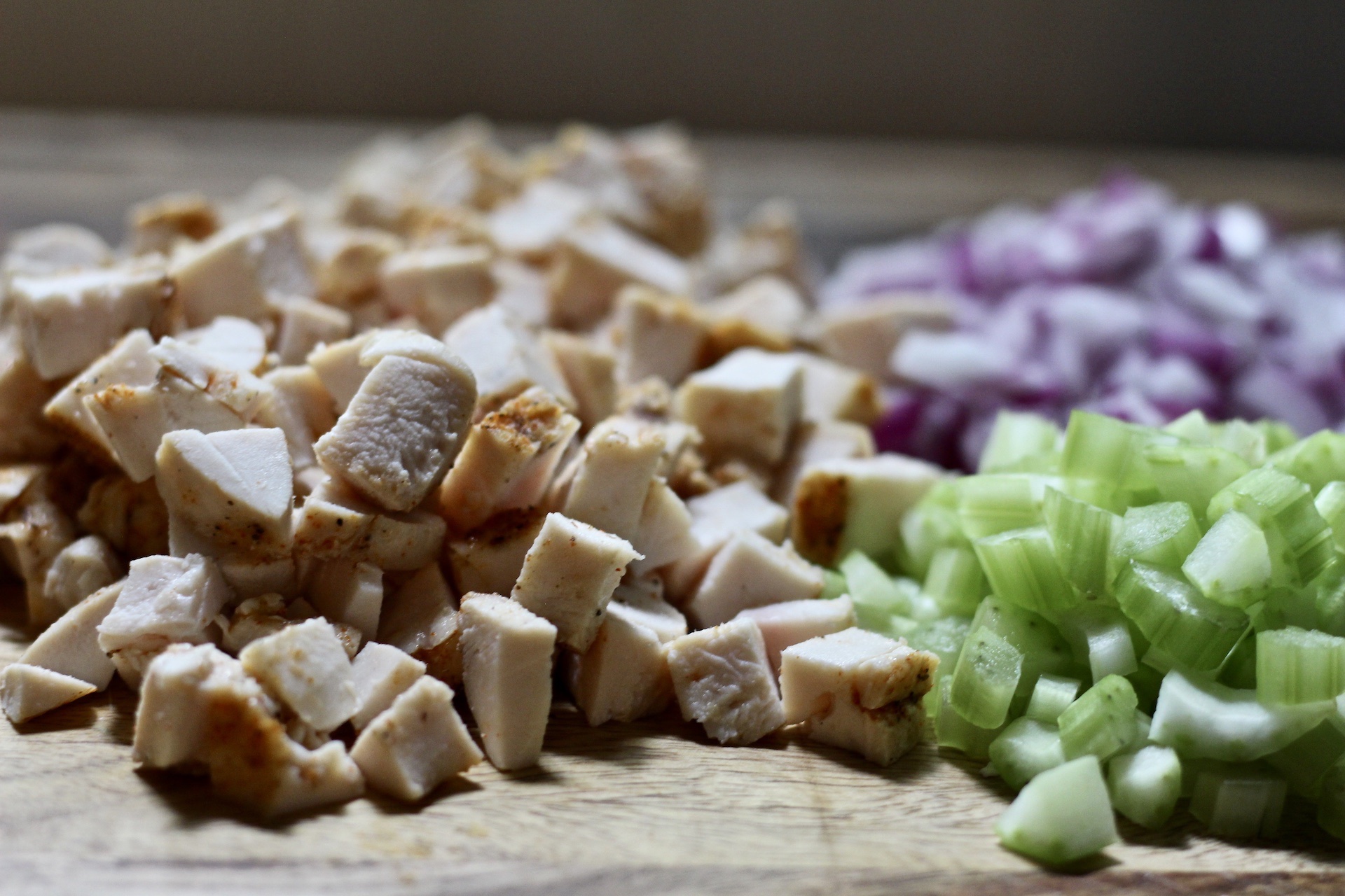 Chopped chicken, celery, and red onion on a cutting board.