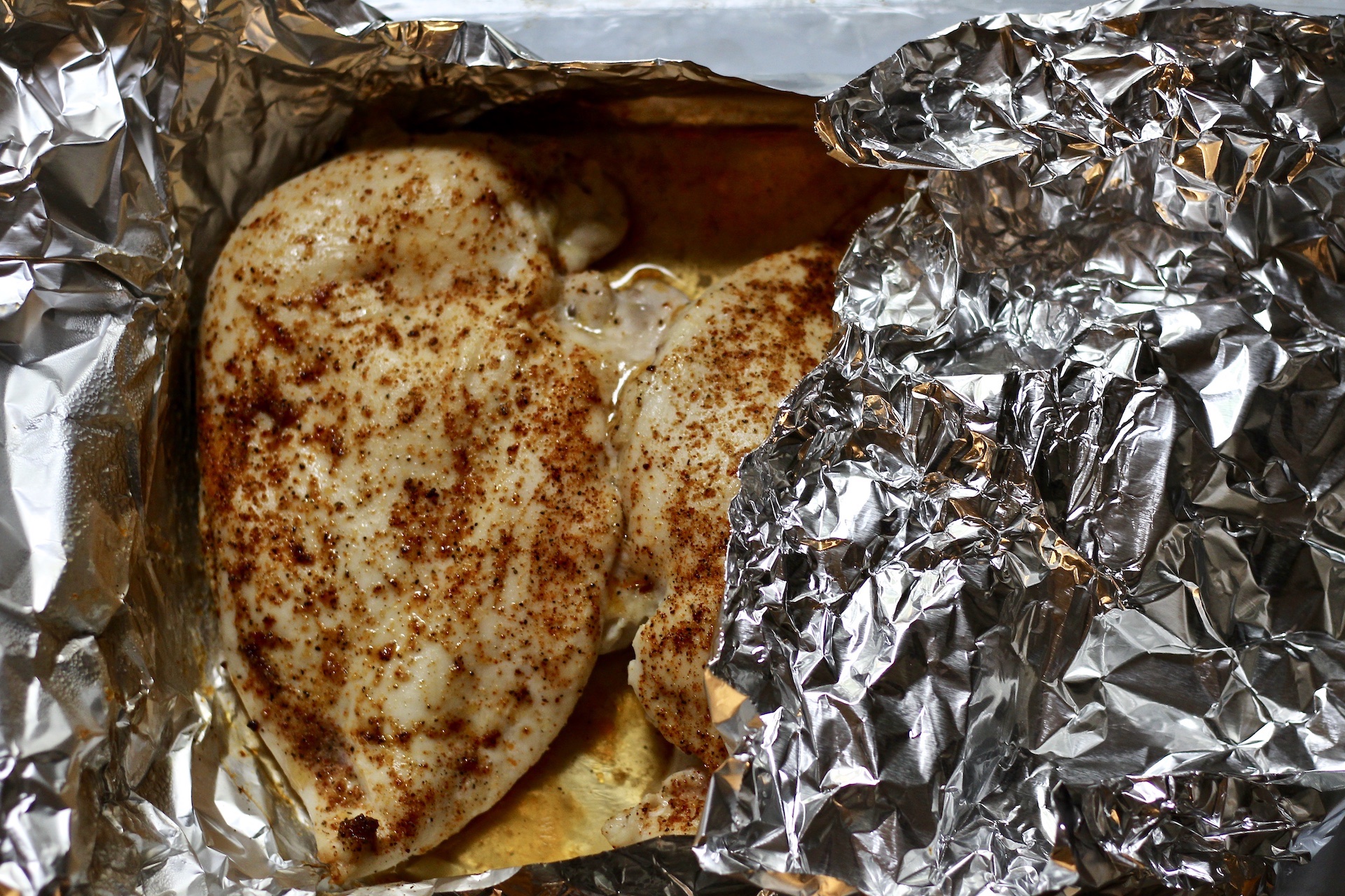 Foil covering the oven baked chicken breasts. One is uncovered.