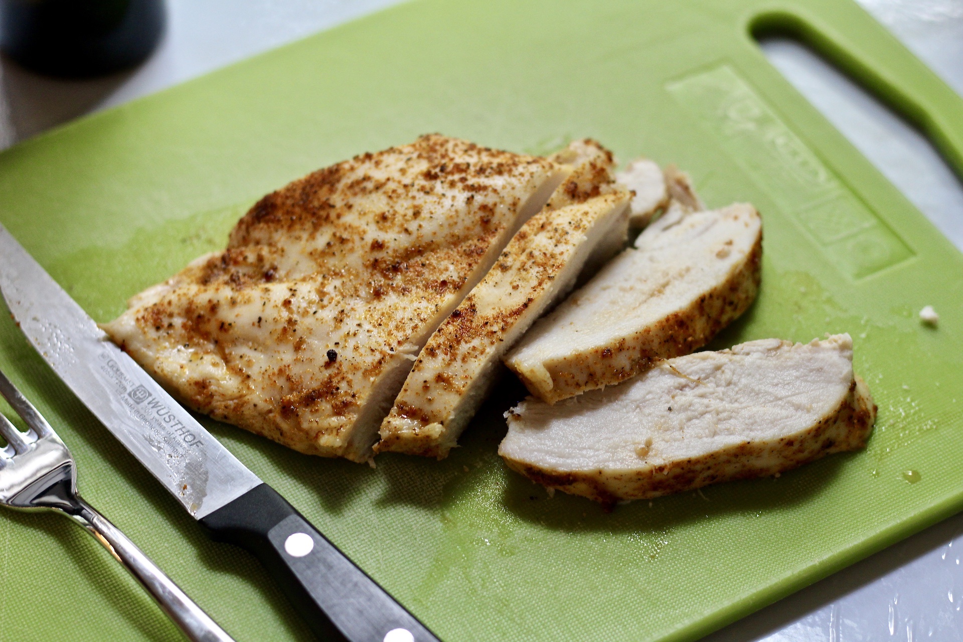Juicy oven baked chicken breast on a green cutting board with a fork and knife. 