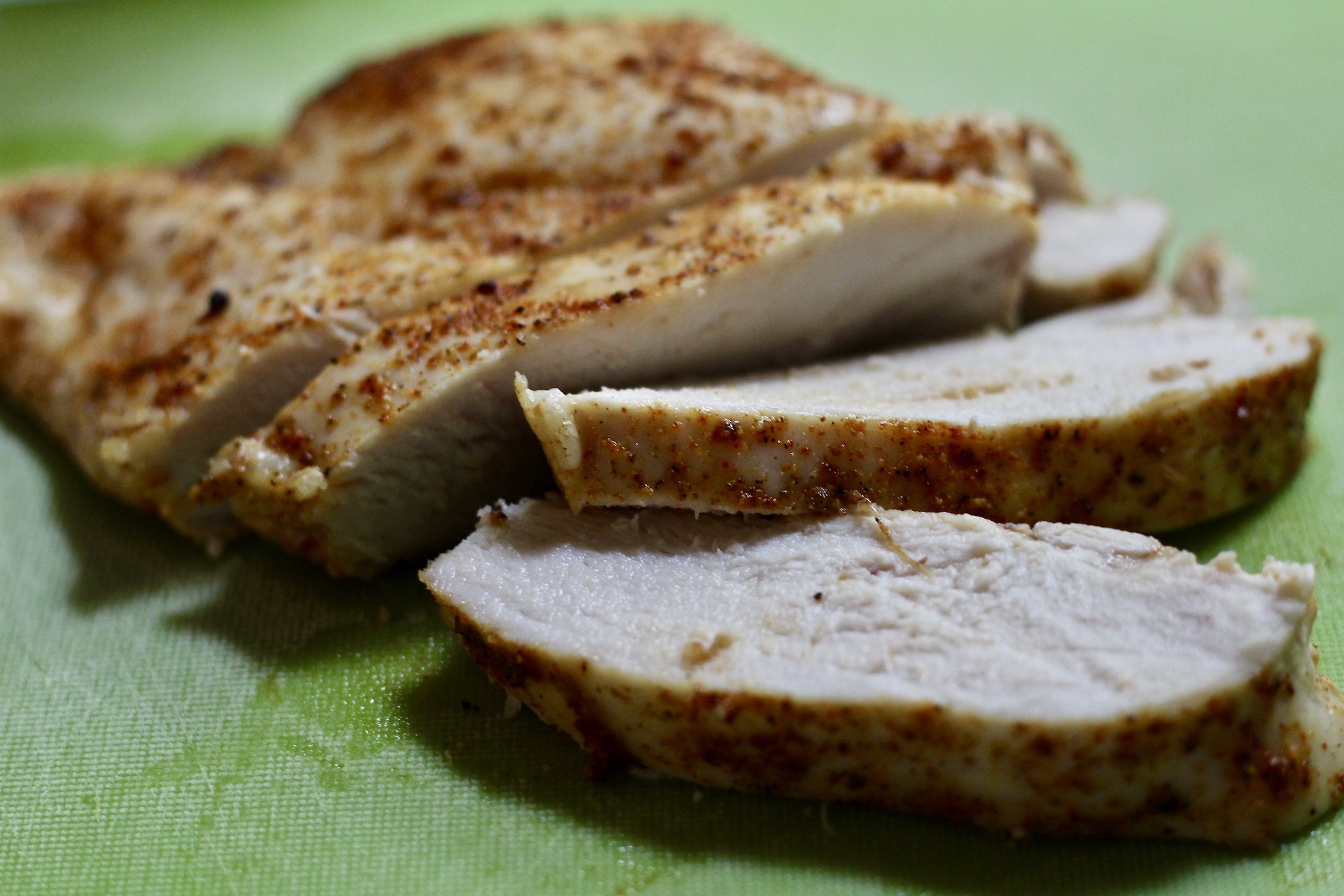 Baked chicken breasts on a green cutting board in slices. 