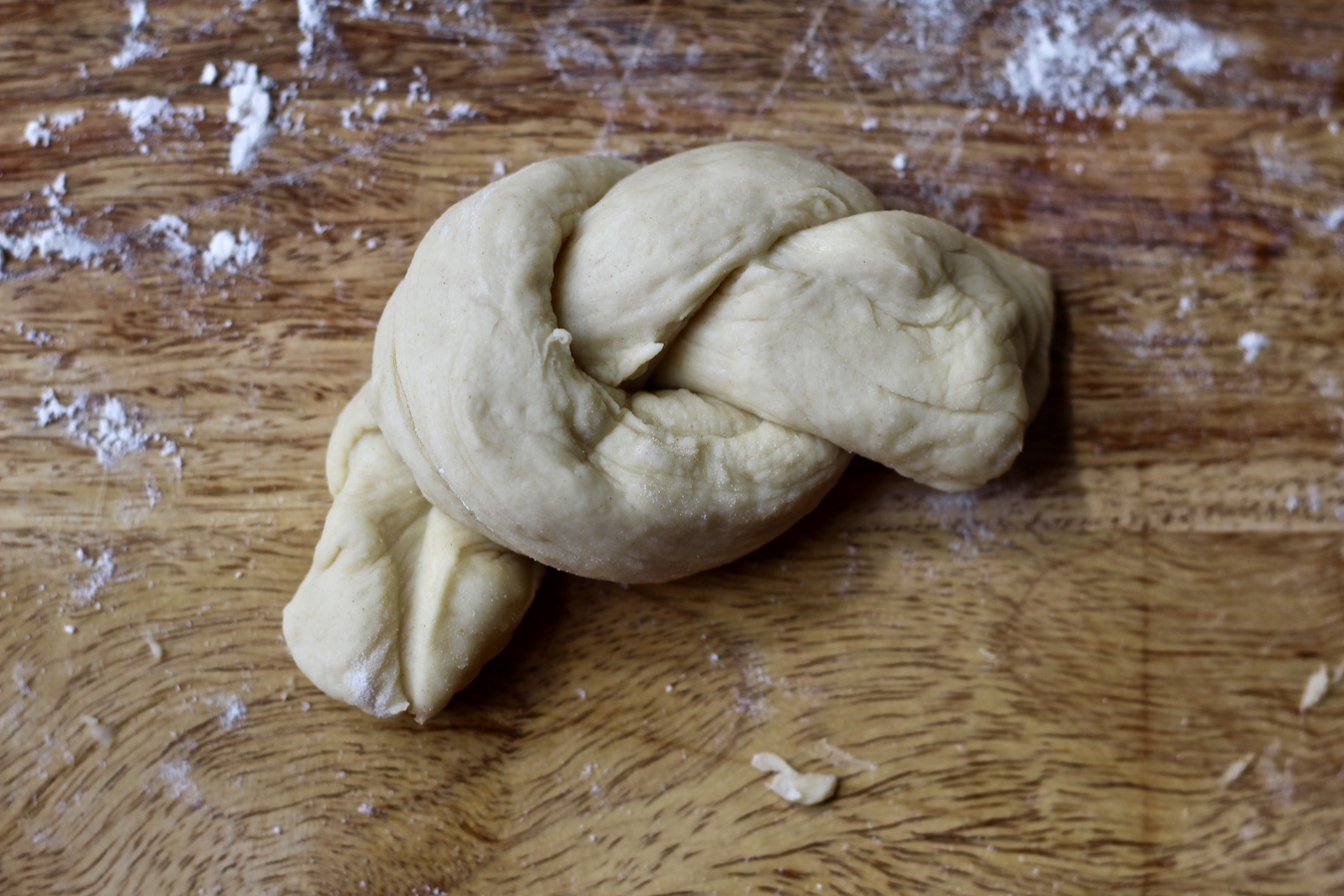 A raw garlic knot on a wooden cutting board after being knotted.