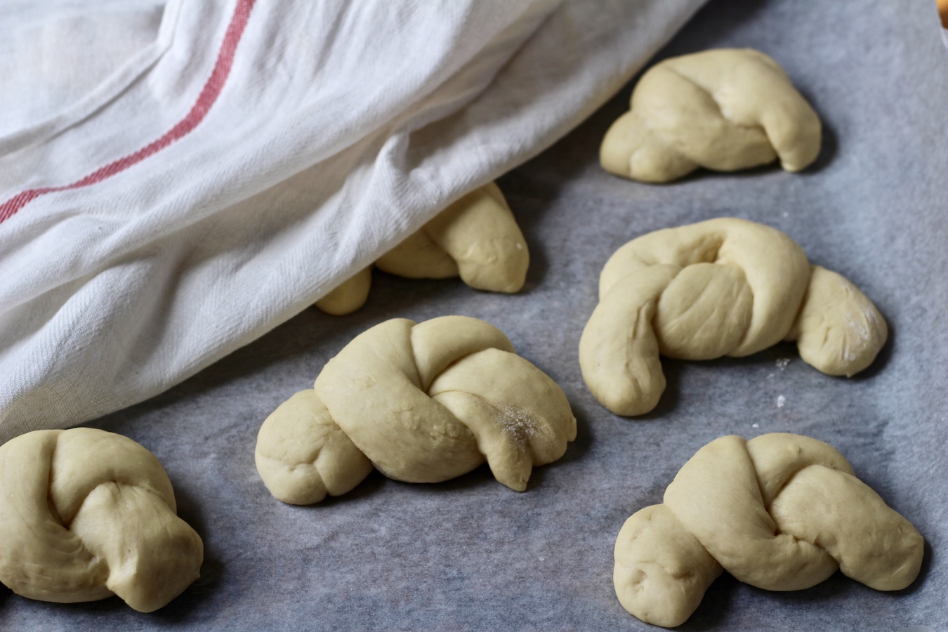Raw garlic knot dough rising under a white and red dish towel.