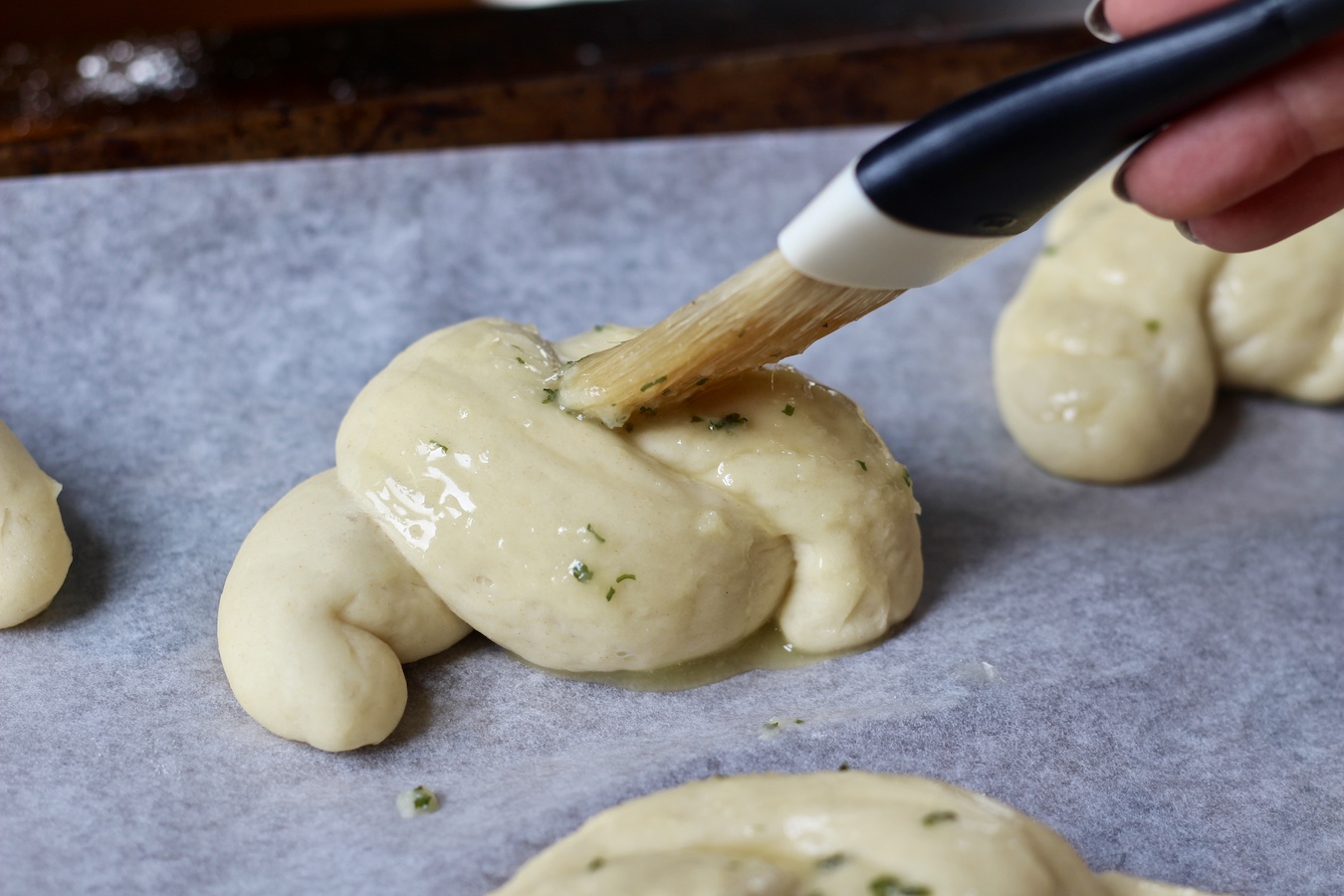 Raw garlic knots being brushed with garlic butter dressing.