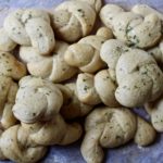 A pile of garlic knots on parchment paper with flour scattered on it possibly.