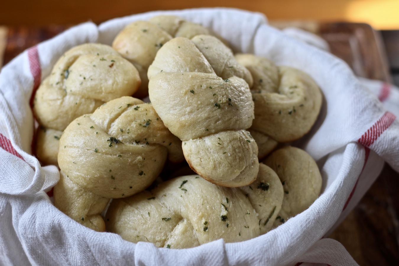 A bowl of garlic knots with a white and red dish towel.