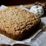 Pumpkin Spice Coffee Cake on parchment paper with little pumpkins in the back.