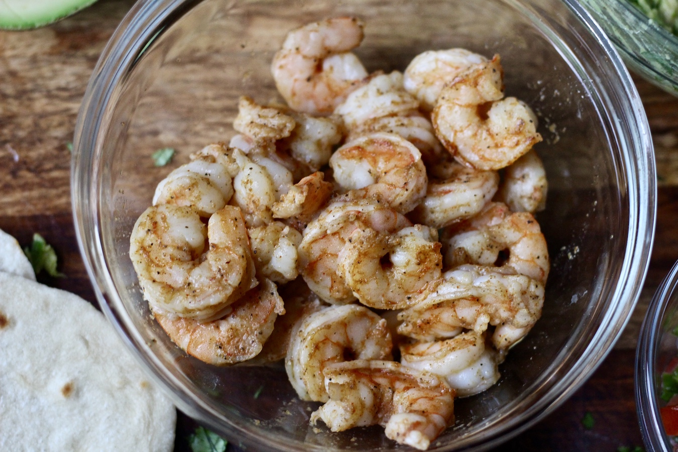Bowl of shrimp for shrimp tacos on a wooden cutting board.