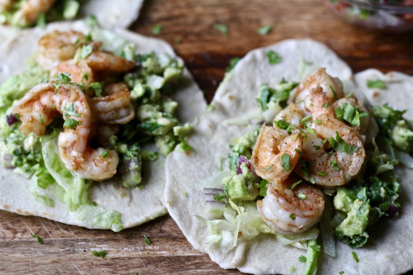 Two shrimp tacos on a wooden cutting board.
