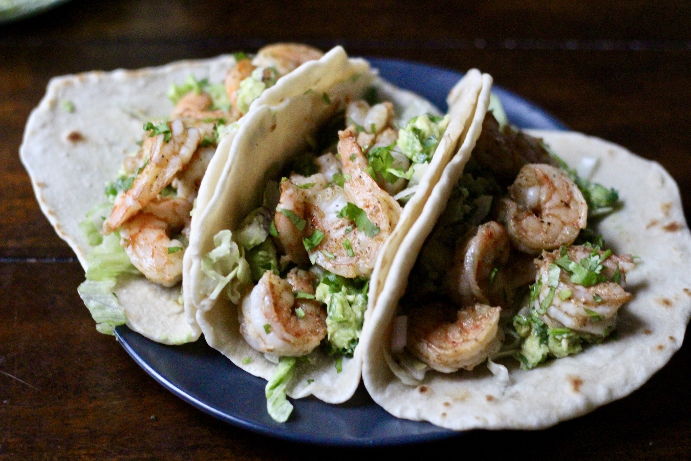 Three shrimp tacos on a dark gray plate.
