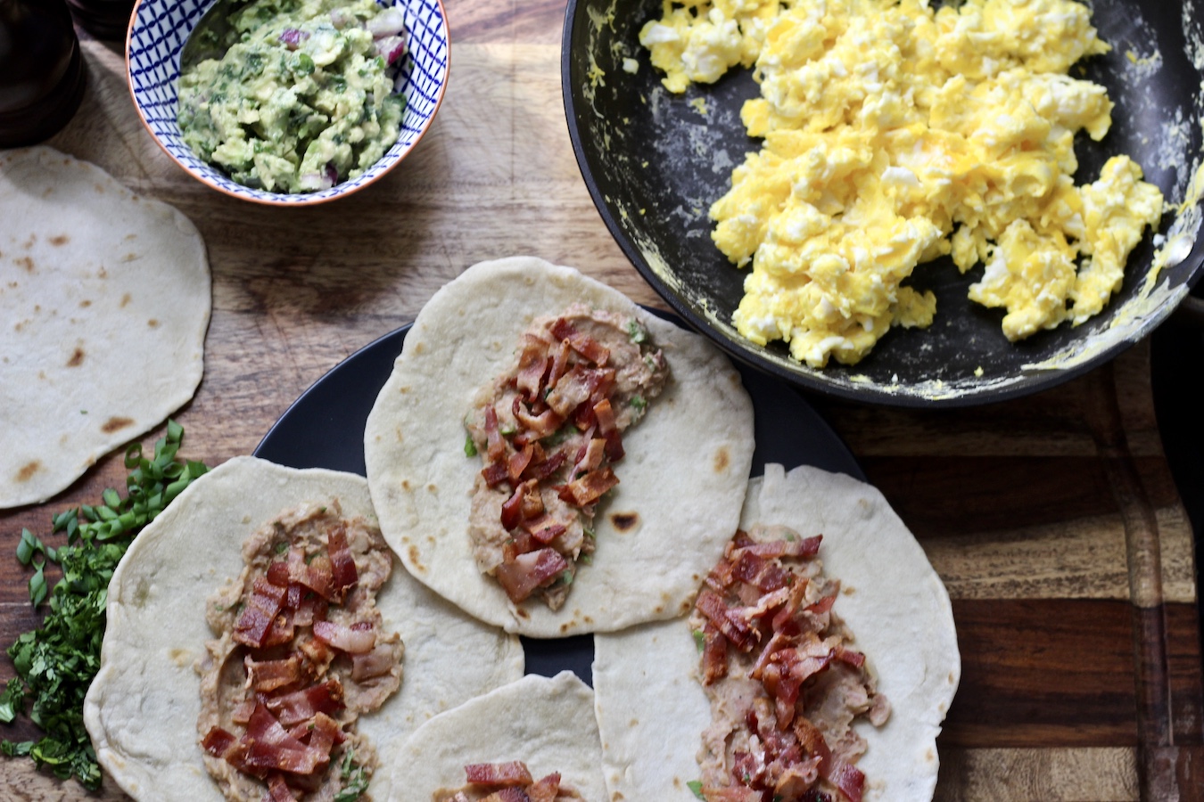 Plate of tortillas with beans and bacon, eggs on the right and guacamole on the left.