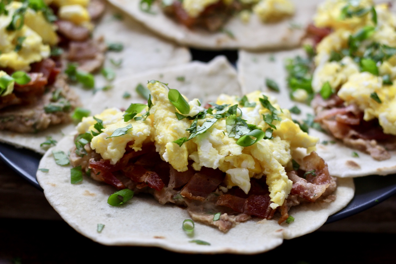 Close shot of a breakfast taco with bacon, eggs, cilantro, and refried beans.