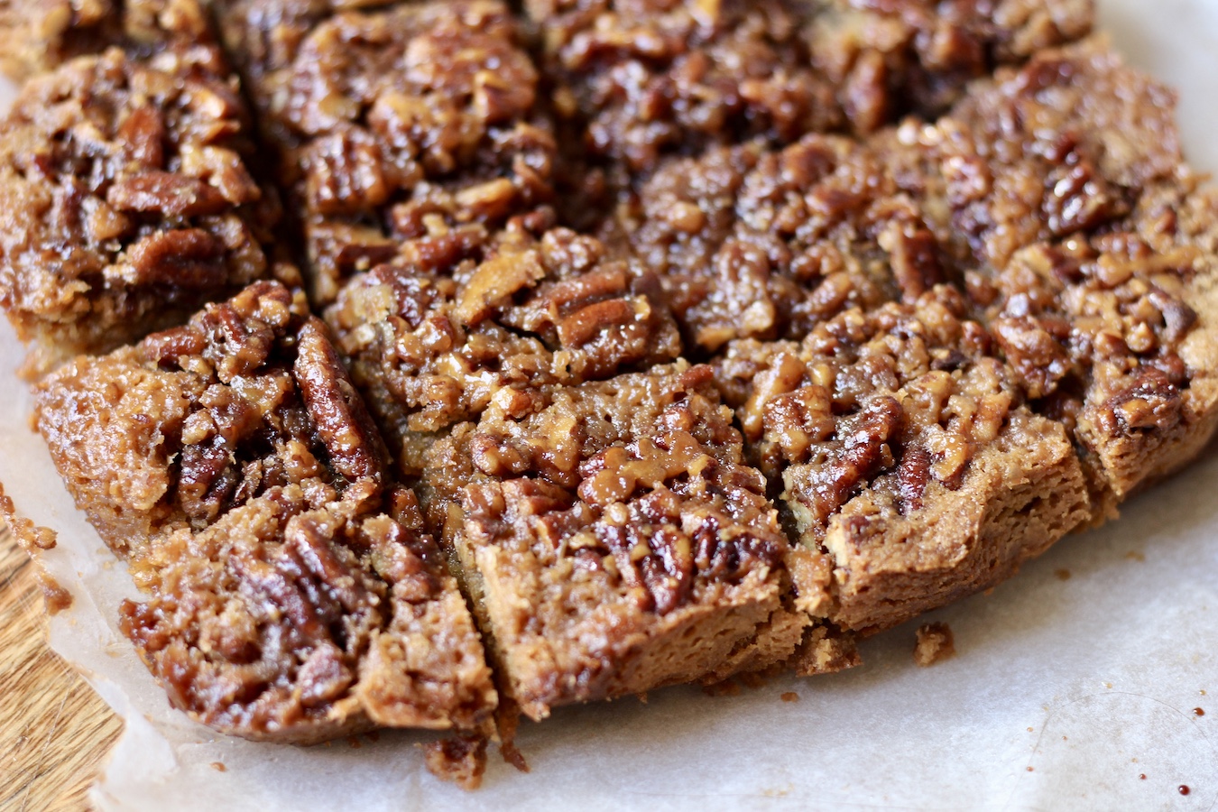 Cut pecan pie blondies on a parchment paper on a wooden cutting board.