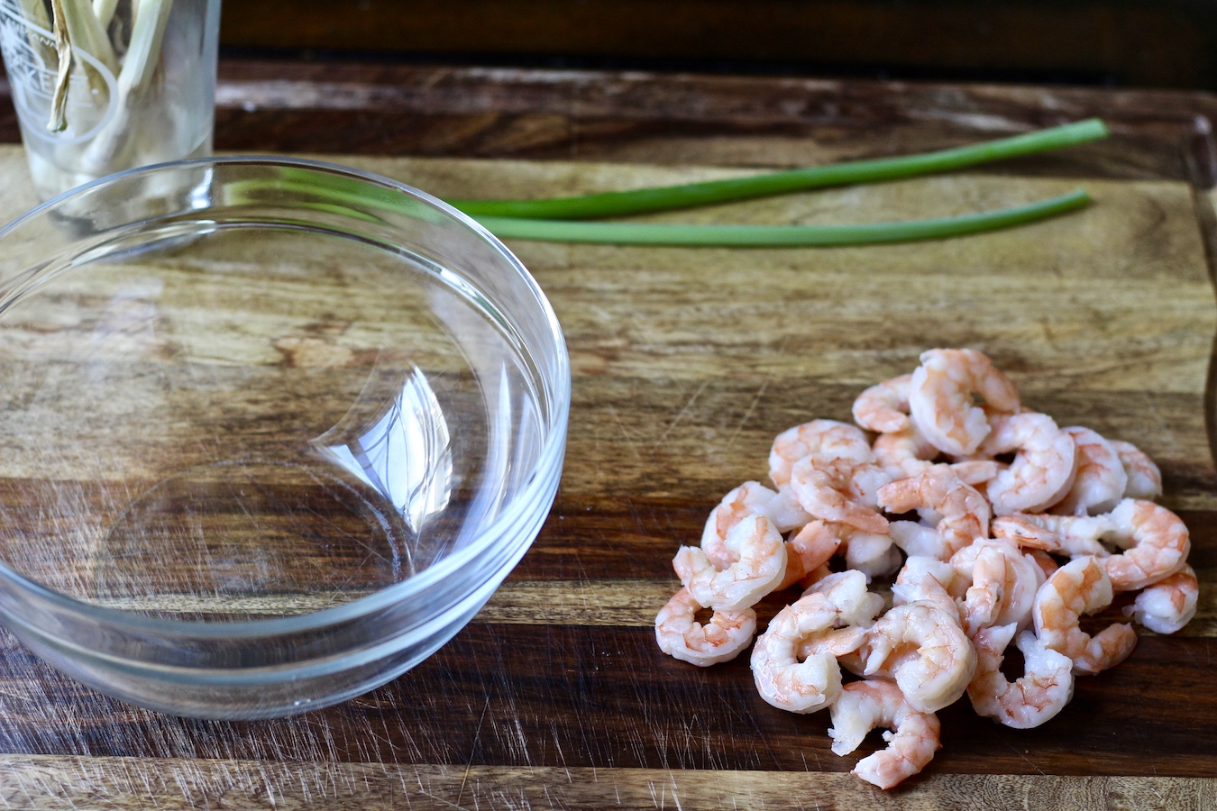 A bowl with cooked shrimp and green onion on a wooden cutting board.