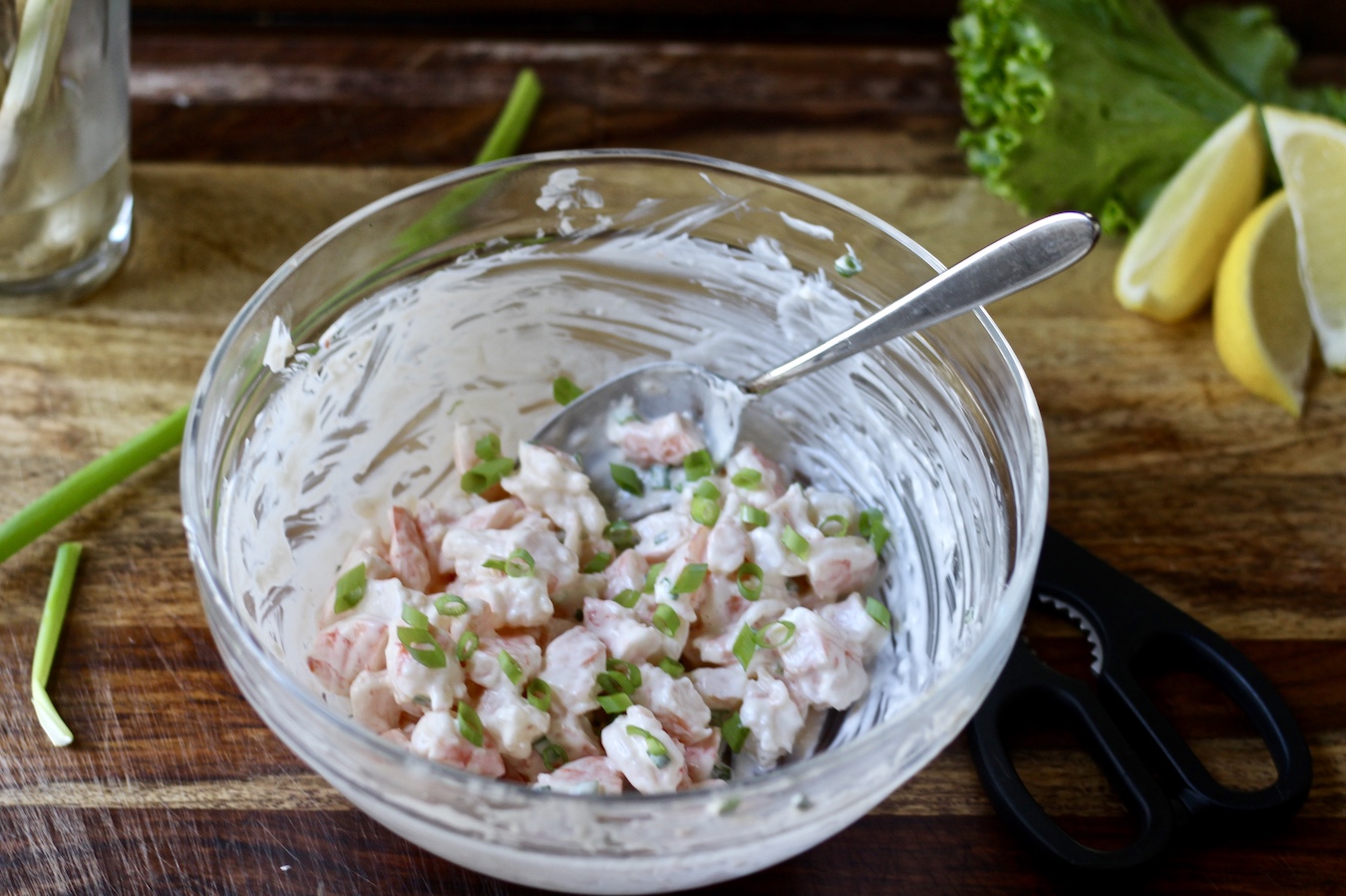 Shrimp rolls filling in a bowl on a cutting board with green onion, lettuce, and lemon.