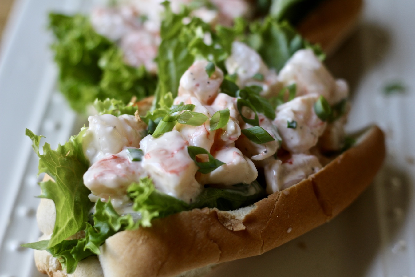 Shrimp roll on a white platter with another shrimp roll behind it.