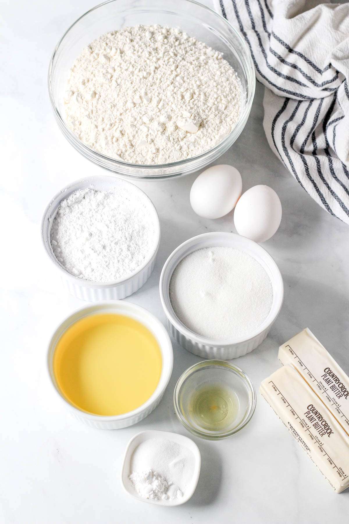 Ingredients for dairy-free sugar cookies on a white counter with a blue and white dish towel to the right.
