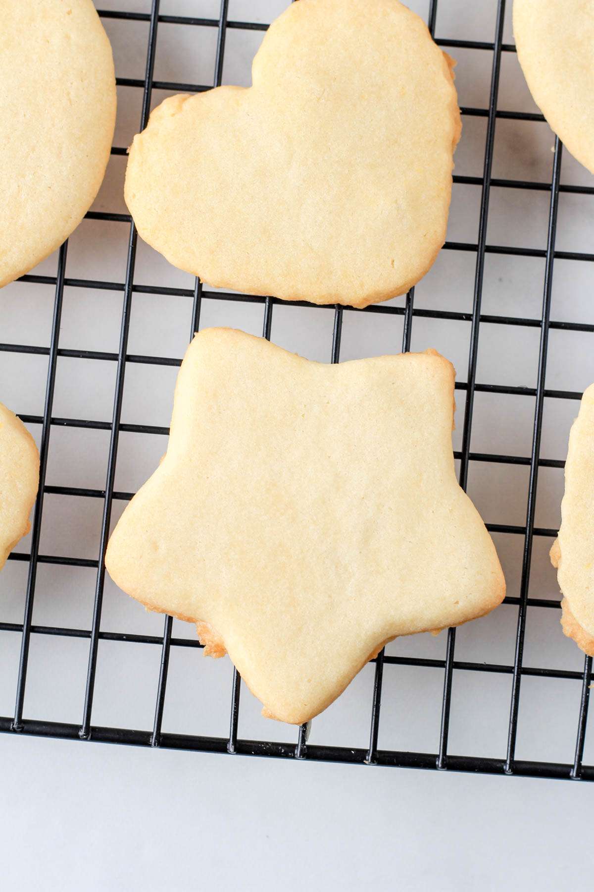 A close up of a star and heart shaped dairy-free sugar cookie on a cooling rack.