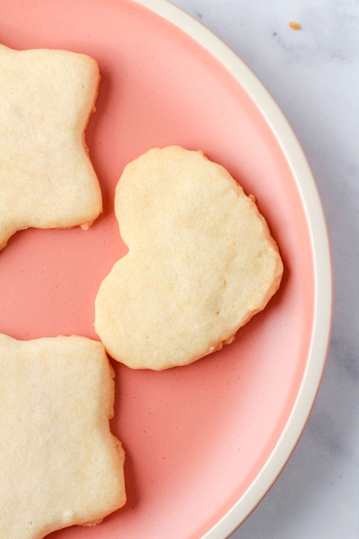 A pink plate with a white rim and three dairy-free sugar cookies on top.