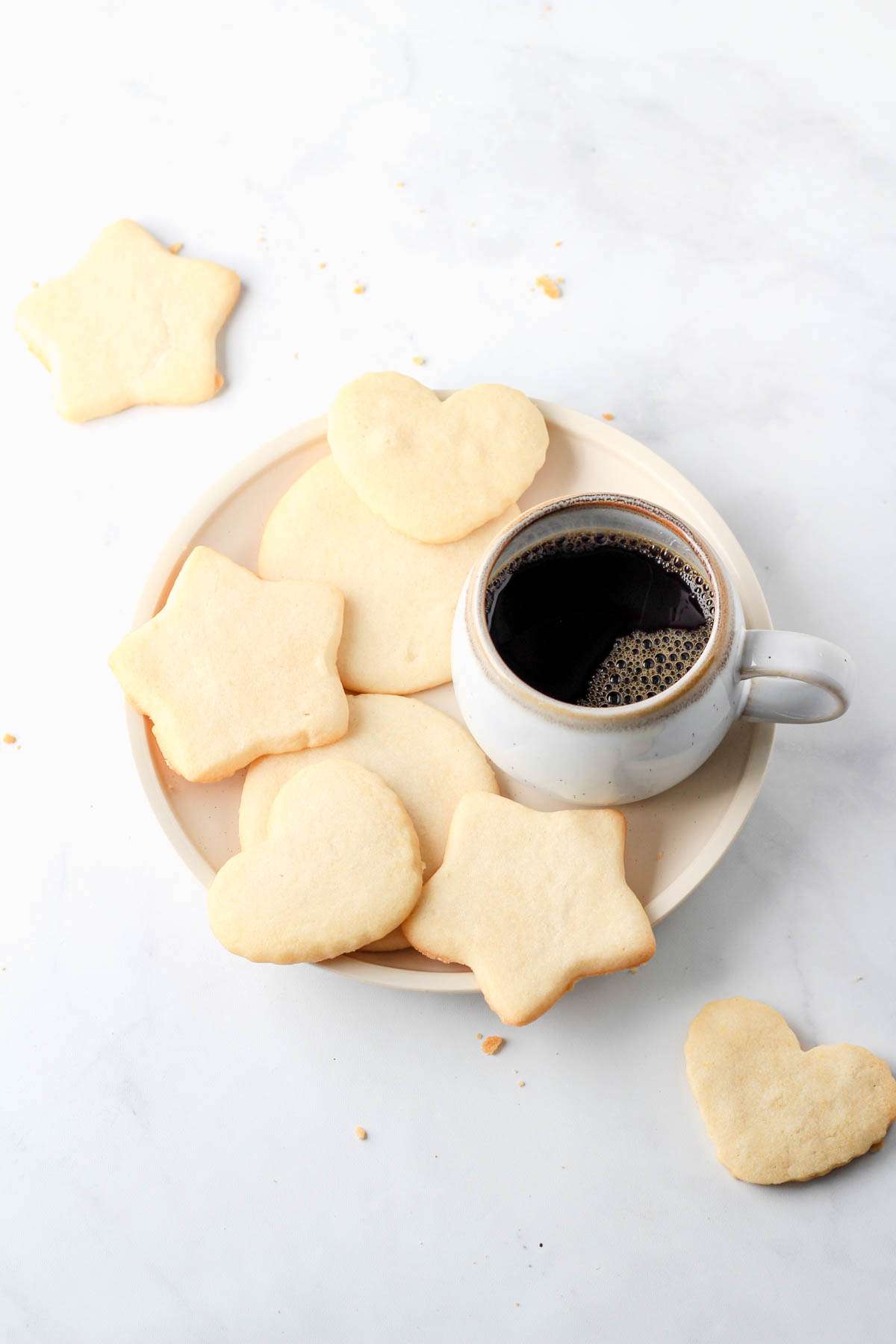 A white plate with dairy-free sugar cookies and a cup of coffee to the right.