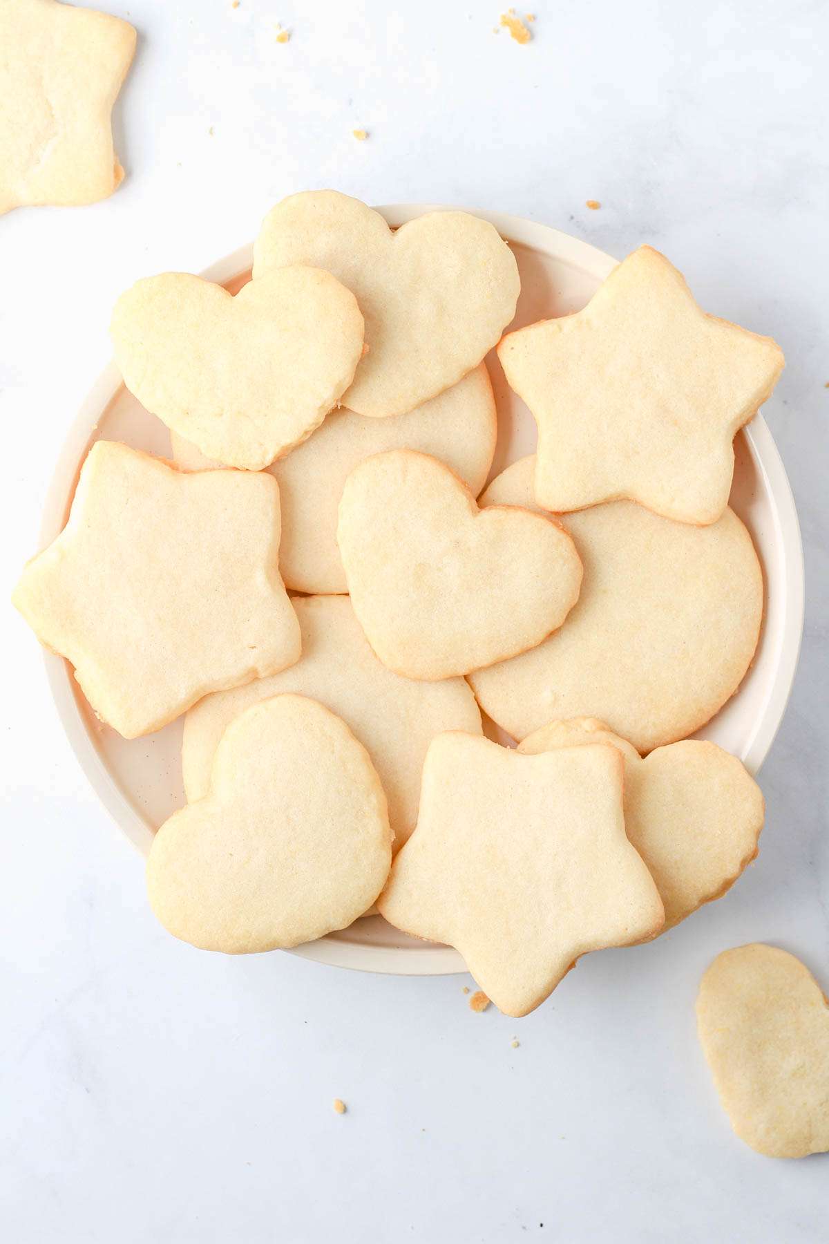 Cut out dairy-free sugar cookies in heart, star, and circle shapes on a white plate.