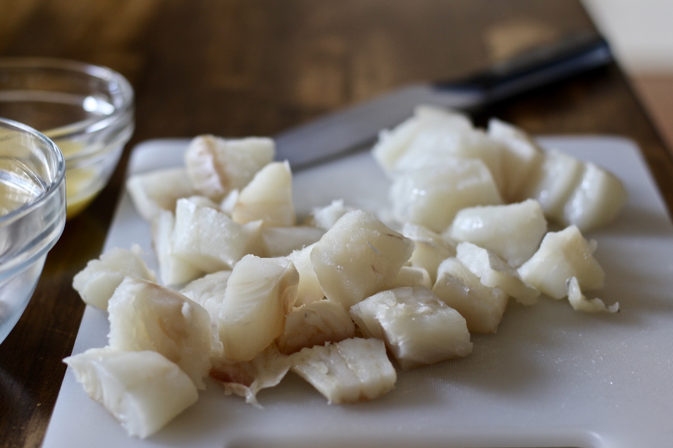Raw white fish on a white cutting board before getting dipped in the egg and bread crumb mixture.