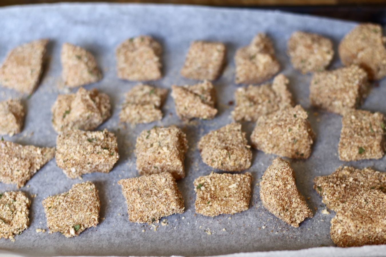 A baking sheet covered in parchment paper with the fish dipped in the egg and bread mixtures.