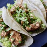 A blue plate with three fish tacos on a wooden table.