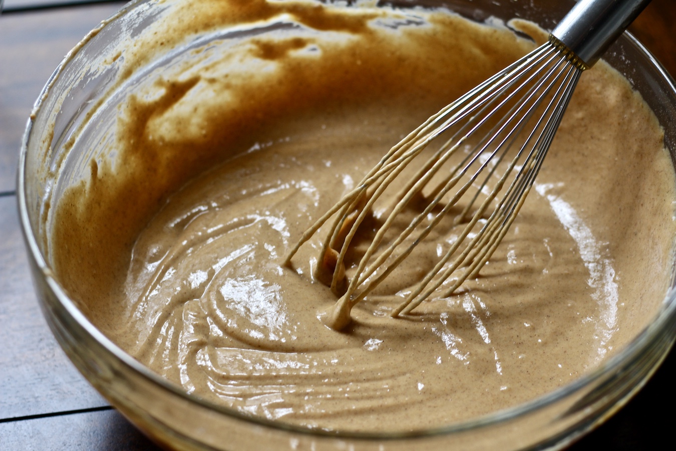 A bowl of pumpkin spice pancake batter with a wire whisk in it.