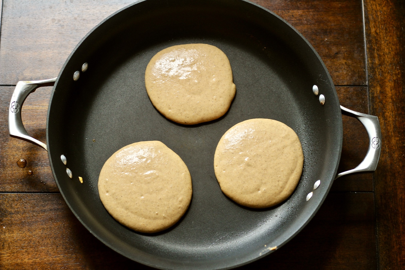 Three pumpkin spice pancakes in a non stick skillet on a wooden table.