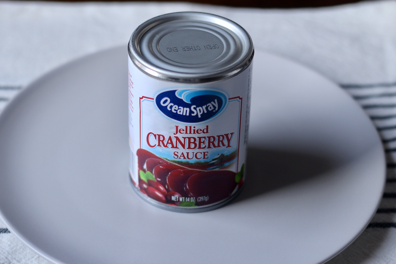 A can of Ocean Spray cranberry sauce on a white plate on a blue and white striped dish towel.