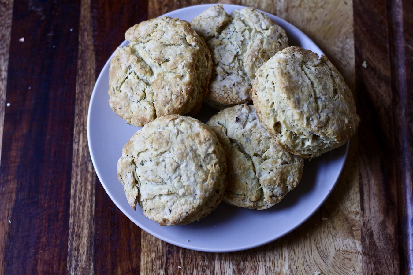 A white plate full of garlic and herb biscuits on a wooden cutting board.