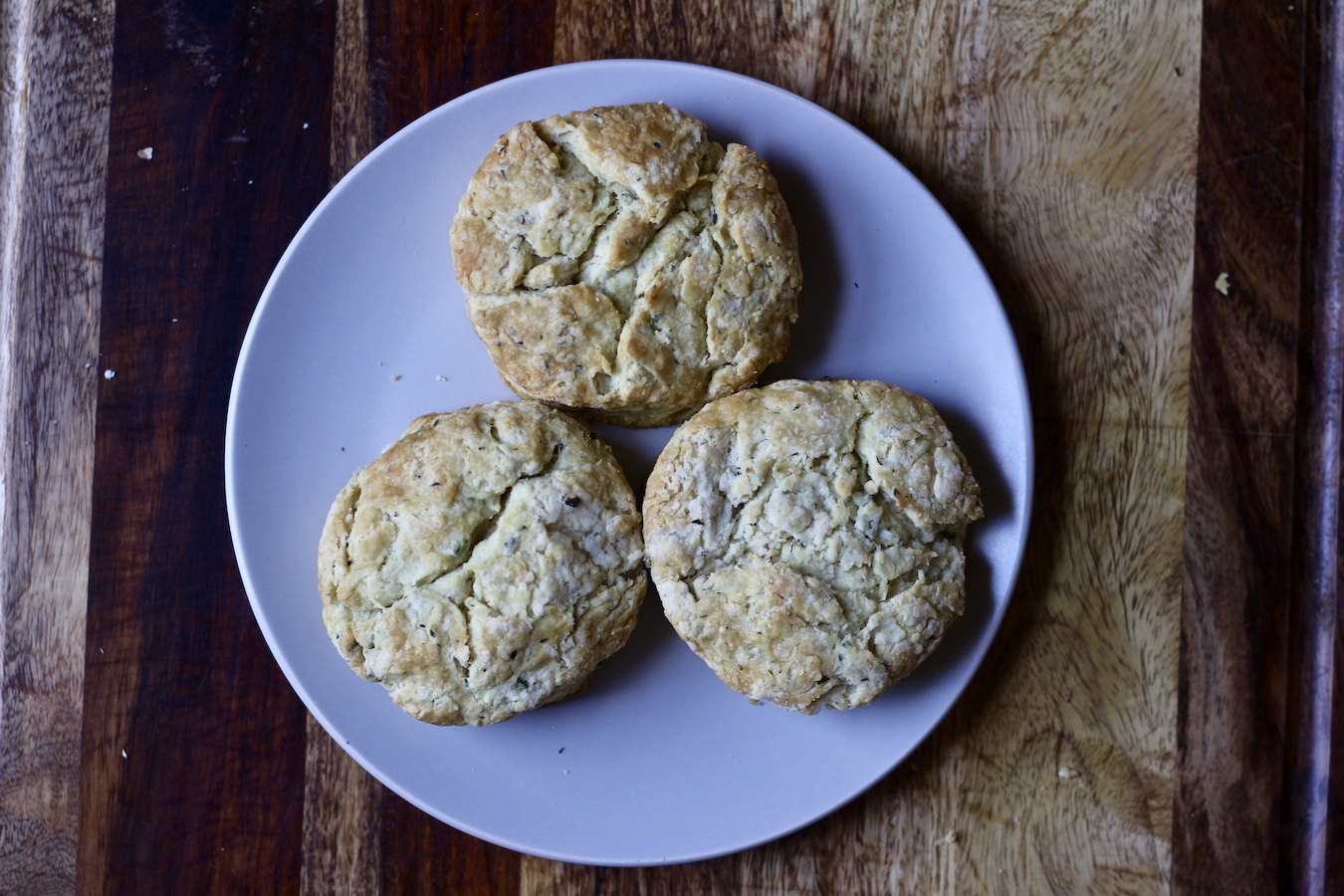 Three garlic and herb biscuits on a white plate in a wooden cutting board.