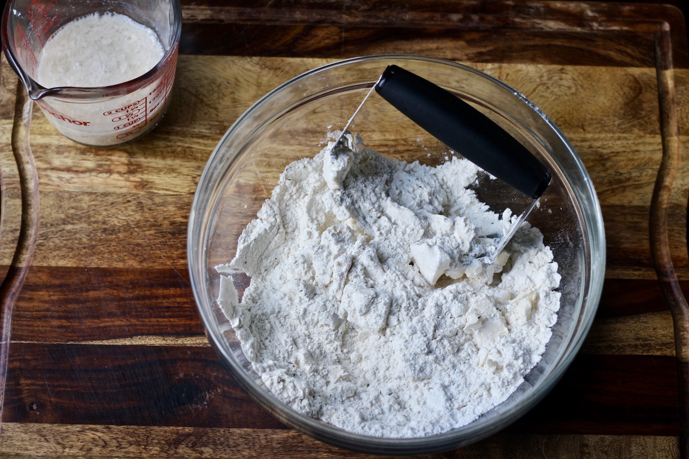 Bowl of flour and herbs with butter being cut in using a pastry blender.