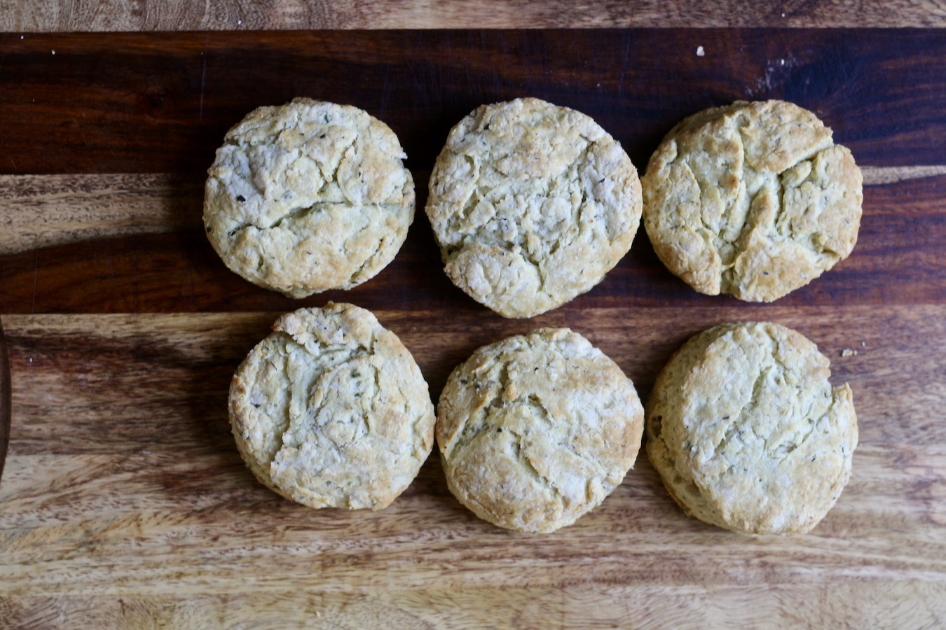 Six garlic and herb biscuits in two rows of three on a wooden cutting board.