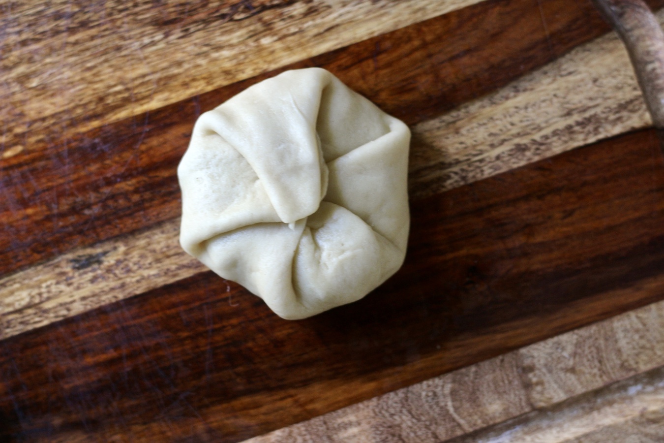 A ball of kolache dough filled with sausage and egg scramble on a wooden cutting board.