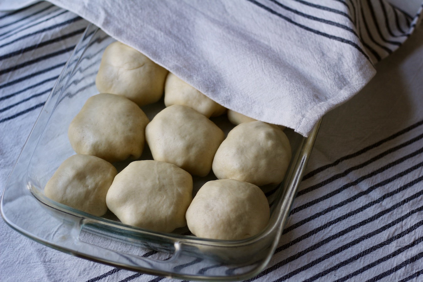 Sausage and egg kolaches in a pyrex dish resting under a white and blue striped towel.