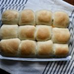 A dozen sausage and egg kolaches in a pyrex dish on a blue a white striped towel.