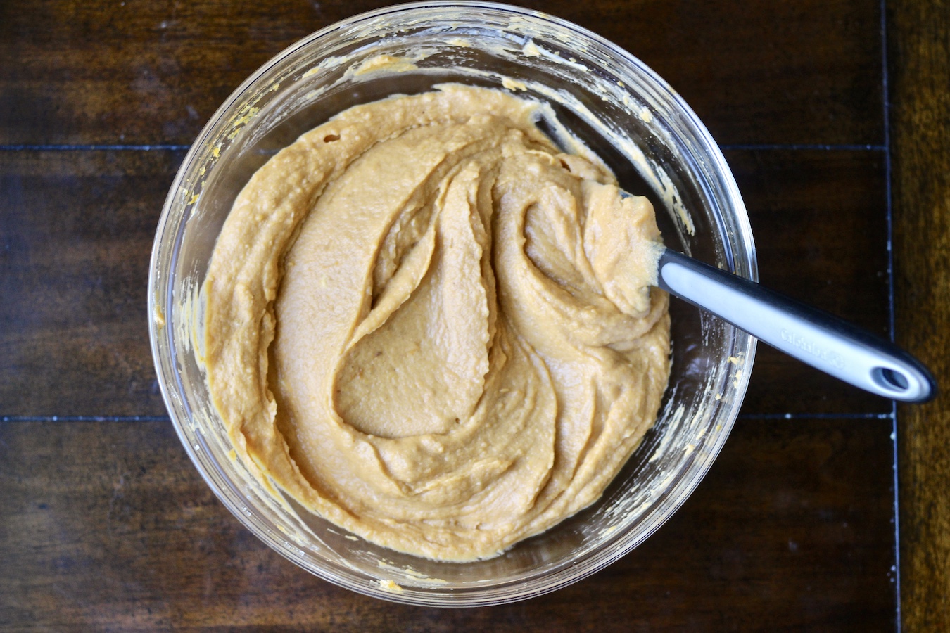 Ingredients for the sweet potato casserole blended in a glass bowl with a rubber spatula.
