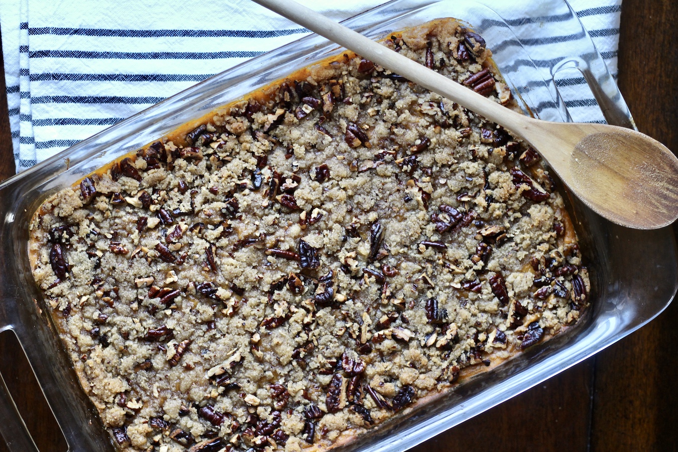 The full pyrex dish of sweet potato casserole with a wooden spoon on top.