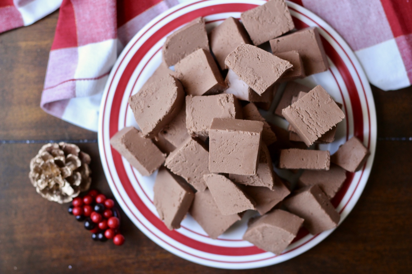 Dairy free fudge piled high on a red and white plate on a wooden table with a red and white checkered towel in the back.