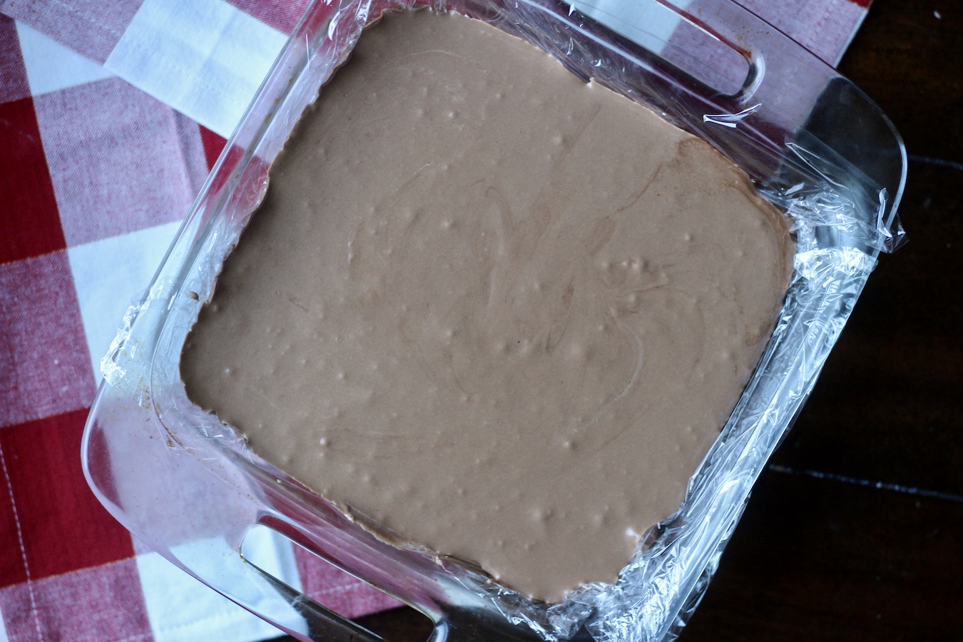 Smooth fantasy fudge poured into the glass dish on a red and white dish towel.